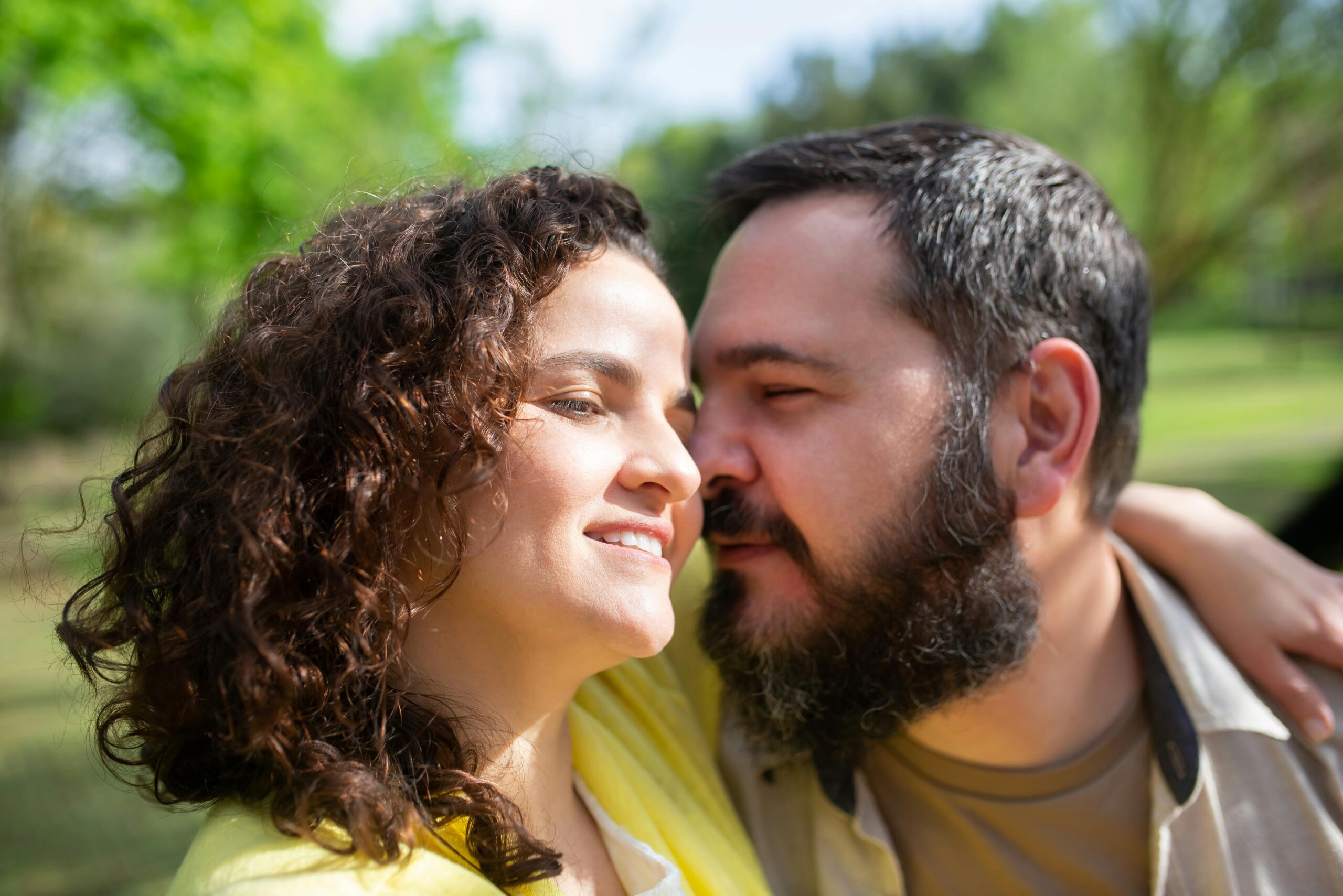 Joyful couple shares an intimate moment in a vibrant green park on a sunny day in Portugal.